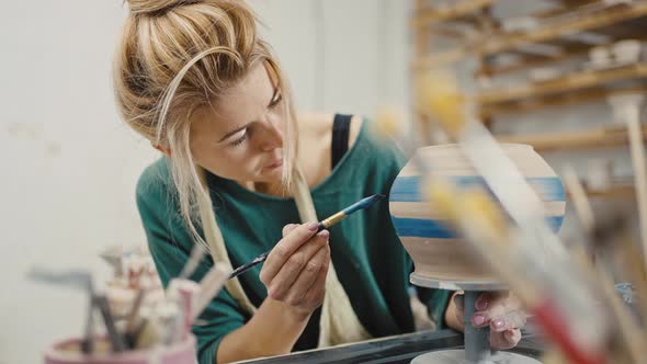 Focused Woman Artist Painting Handmade Ceramic Pot with Blue Dye Sitting at Pottery Workshop Slow