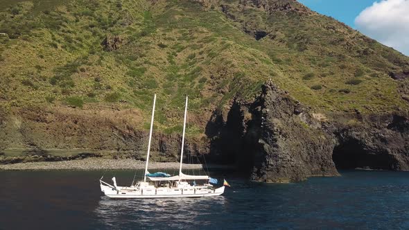 Aerial View on White Sailing Catamaran with Flags of Ukraine and Europe Union Against Rock of Lipari