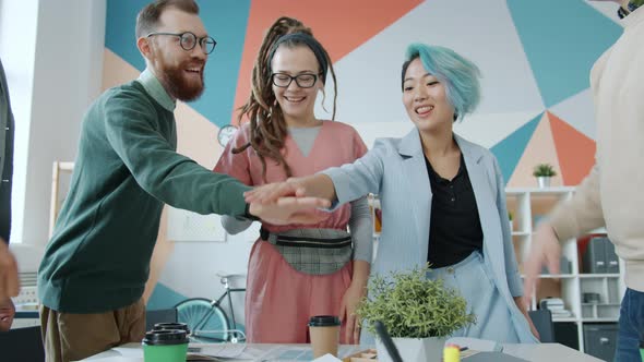 Multi-ethnic Team of Colleagues Joining Arms Celebrating Unity and Success in Office