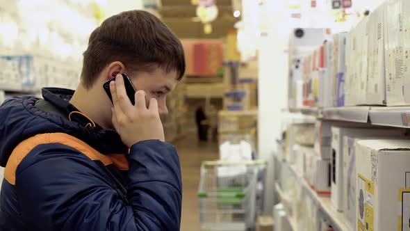Young Guy Is Talking on the Phone, Standing in Electrical Goods Department, Chandeliers, in the