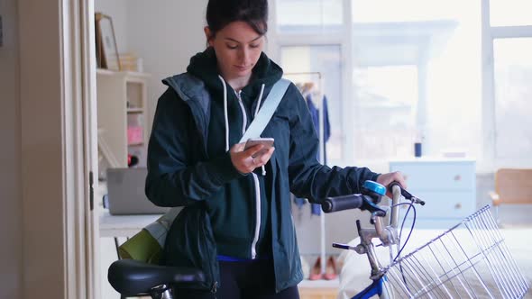 Woman using her mobile phone while taking her bicycle out