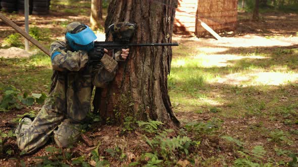 Man Wears Camouflage and Protective Mask While Participating in a Paintball Battle Game with Friends