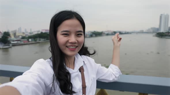 Beautiful young Asian female video chatting with her friends while standing on the Rama VIII Bridge.