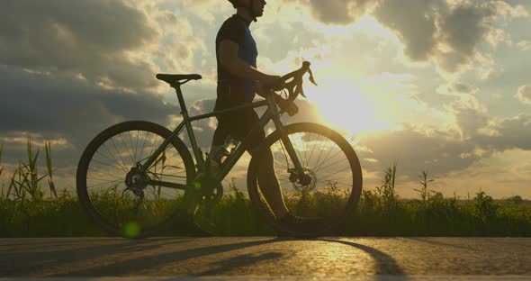 A Sportsman is Walking Along the Road with a Bicycle