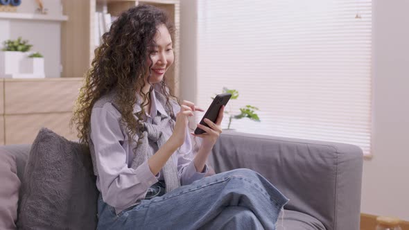 Asian woman Sitting on the sofa in the house, an Asian man works on his tablet.woman works while usi