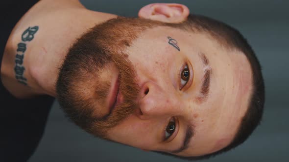 Closeup Young Bearded Caucasian Man with Tattoos on Face and Neck Dark Background