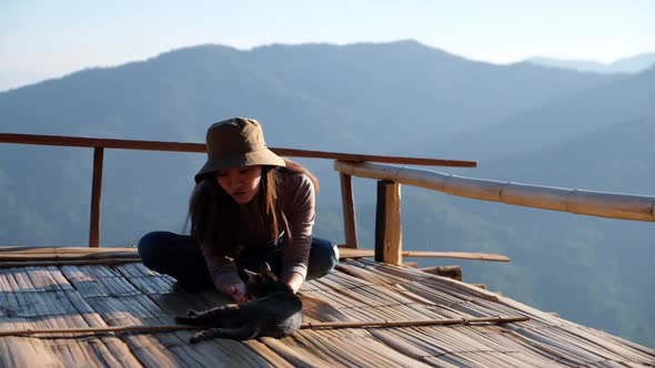 Slow motion of a female traveler sitting and playing with cat on wooden balcony