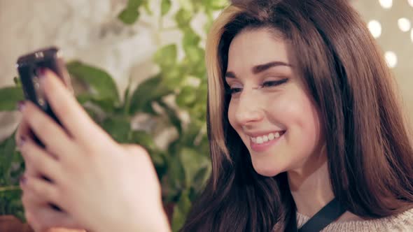 Young Brunette Woman in Harness at Cafe Using Mobile Phone Reading Messages Smiles and Starts