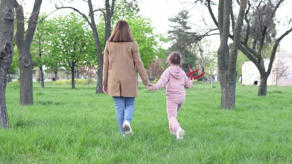 Happy mom and teen daughter having fun outdoors, carefree family playing with red airplane toy model