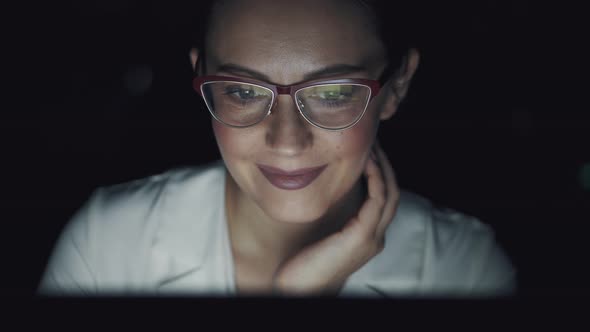 Reflection of the Monitor Screen with Glasses. Young Woman Working Late in the Office