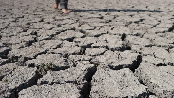 Barefoot man walks on dried soil.