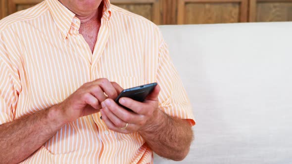 Senior man using mobile phone in living room