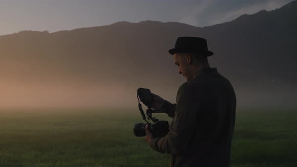 Man Adjusting Camera With Monitor In Misty Field At Sunrise