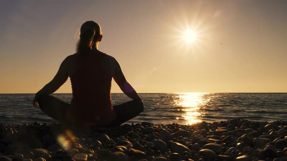 Silhouette of girl engaged in yoga sitting on seashore at sunset