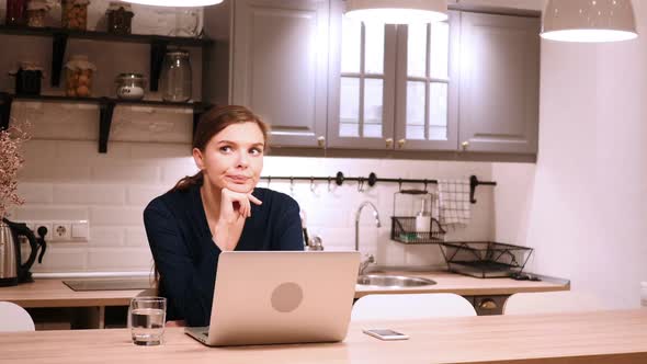 Pensive Woman Thinking and Working Online in Kitchen