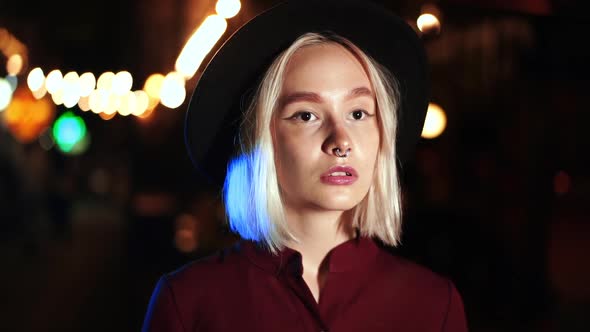 Portrait of Trendy Hipster Woman with Blond Hairstyle Standing on City Street at Night. Hat, Nose