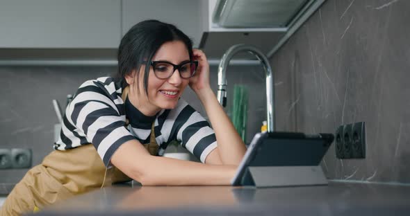 Young Caucasian Smiling Woman in Eyeglasses Using Internet on Tablet Device During Home Routine