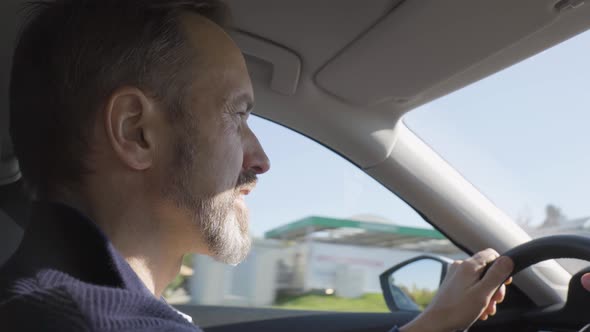 A Middleaged Handsome Caucasian Man Drives a Car Through an Urban Area  Side Closeup