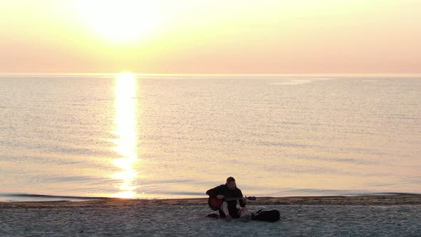 Man playing the guitar on the beach at sunset - aerial view