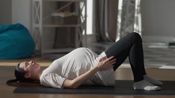 Side View Concentrated Pregnant Sportswoman Raising Hips Lying on Exercise Mat at Home