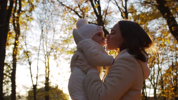 Happy mom spinning with her baby on the background of sunset and foliage