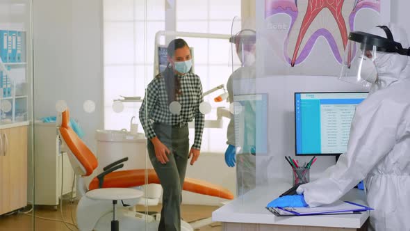 Doctor with Protection Suit Inviting Next Patient in Dental Room