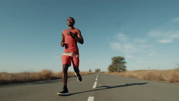 Black Man of Athletic Build in Sportswear Runs Along an Asphalt Road Outdoor Front View