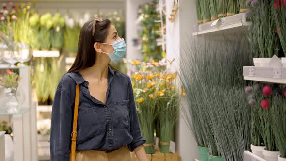 Woman in Face Mask Looking at Green Decorative Artificial Potted Plant for Home Decor