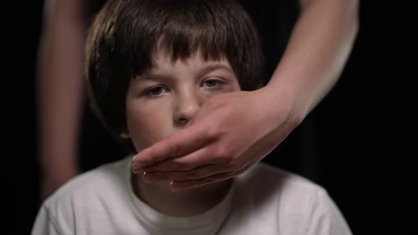 Closeup Front View of Caucasian Boy Looking at Camera As Female Hand Closing Mouth