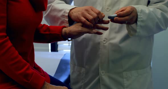 Mid section of young Asian male doctor measuring blood sugar level with glucometer of senior woman i