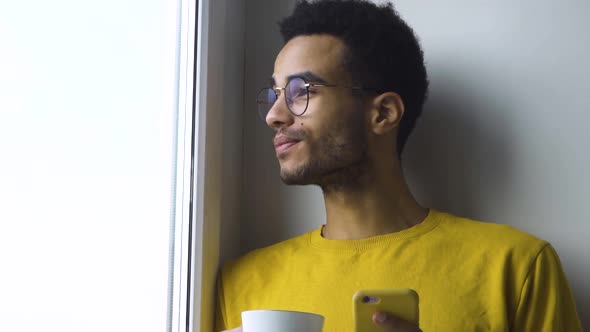 African Guy Drinking Coffee From a Mug By the Window