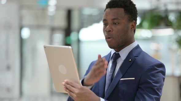 Video Call on Tablet By African Businessman in Modern Office