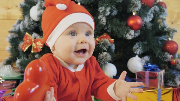 Child in a Suit of Santa Claus Plays Near the Christmas Tree