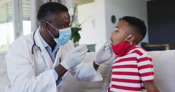 African american doctor wearing face mask taking a throat swab sample of boy at home