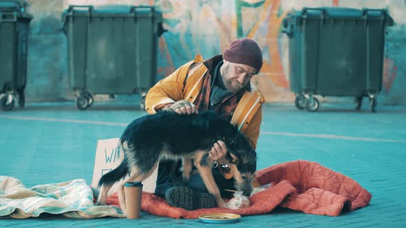 A Tramp is Petting His Dog While Sitting on the Ground