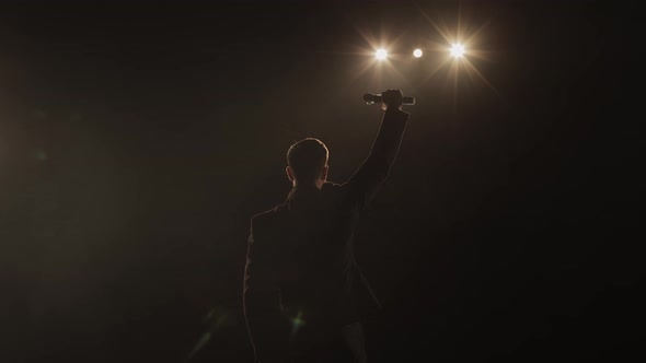 The Man is Standing on Stage and Raising Up the Microphone