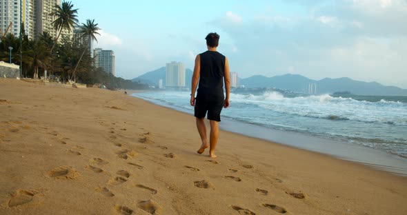 Young Caucasian Man Walking on the Sand Along the Shore Outdoors Against the Backdrop of the
