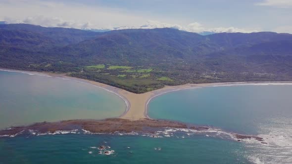 Aerial shot pulling away from the whale tail shaped rocky point of Punta Uvita surrounded by bright