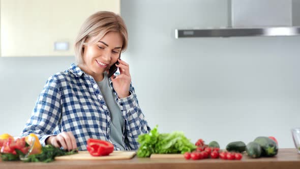 Relaxed Young Smiling European Woman Talking Using Smartphone During Cooking Healthy Food