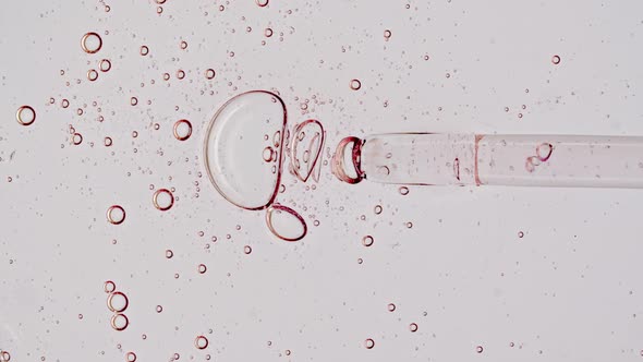 Transparent Pink Cosmetic Gel Fluid Serum with Molecule Bubbles Oil in Pipette Drips on a White