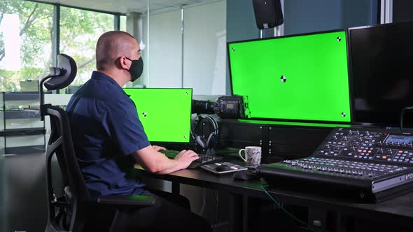 Caucasian man working in video edit suite with multiple screens, chroma key