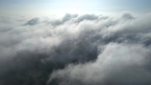 Aerial shot of flying over a layer of soft clouds at dawn