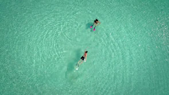 Aerial view of man and woman swimming with masks and flippers in clear sea.