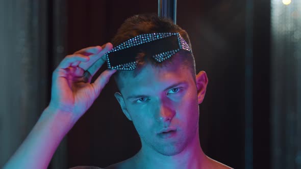 A Young Man Stripper Acting Sexy in Neon Lighting  Putting on Glasses Covered in Rhinestones