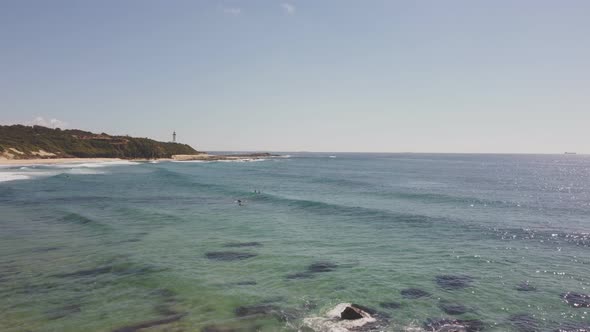 ascending aerial shot of pebbly beach with norah head lighthouse in the distance