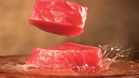 Super Slow Motion with Splashes of Water Falling Tuna Steaks on a Wooden Cutting Board