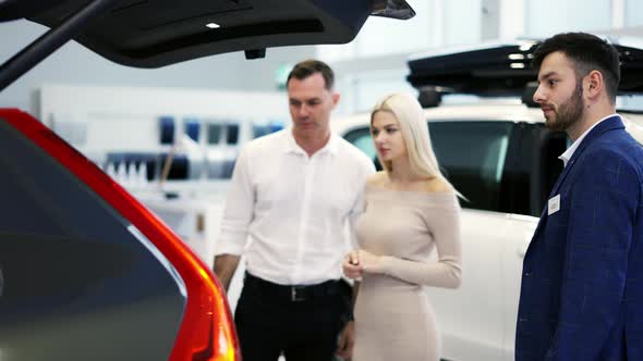 Car Agent Showing Trunk to Customers Car in Automotive Dealership Showroom