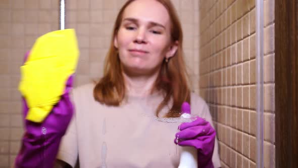 Woman in Gloves with Detergent Spray Rag Washes a Partition in the Shower