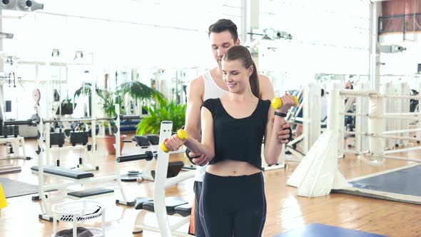 Male Trainer Assisting Woman Lifting Dumbbells.