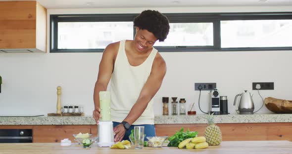 Fit african american man cooking, preparing healthy green smoothie